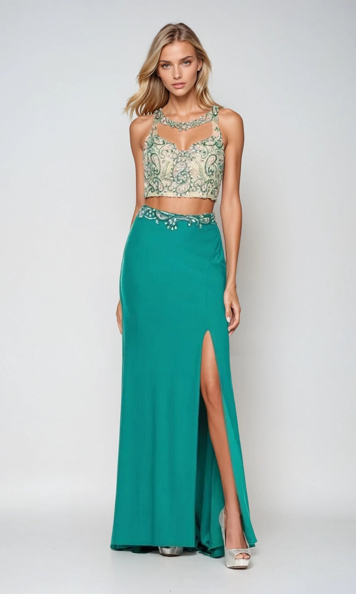 A woman wearing the Juliet 595 long prom dress with a beaded top and teal skirt featuring a side slit stands against a plain background.